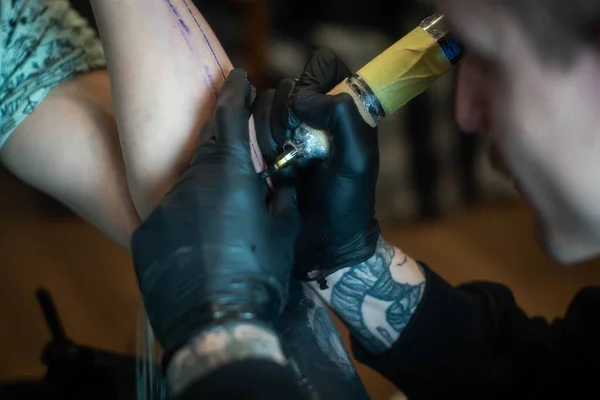 cropped shot of tattooing process on hand in salon. A professional tattoo artist introduces ink into the skin using a needle from a tattoo machine.Professional tattooist working in studio.