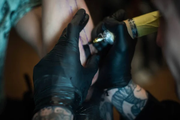 cropped shot of tattooing process on hand in salon. A professional tattoo artist introduces ink into the skin using a needle from a tattoo machine.Professional tattooist working in studio.