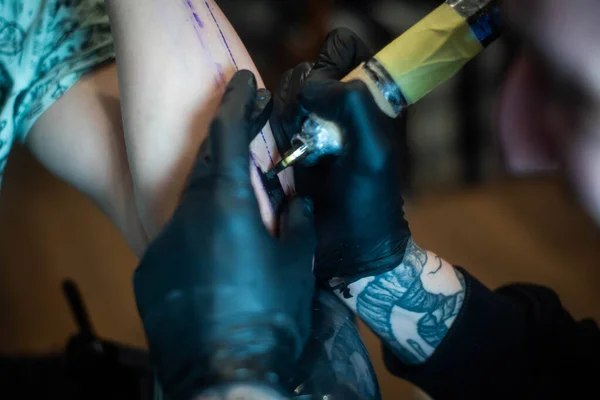 cropped shot of tattooing process on hand in salon. A professional tattoo artist introduces ink into the skin using a needle from a tattoo machine.Professional tattooist working in studio.