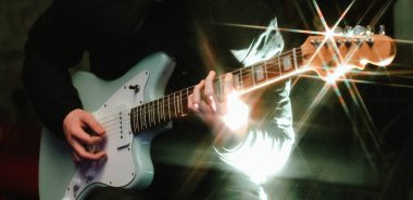 Genç adam elektro gitar ile ışık efekti koyu arka plan üzerinde oynamak