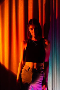 Kot pantolon ve siyah tişörtlü genç ve seksi kadın renkli neon ışıkta poz veriyor.