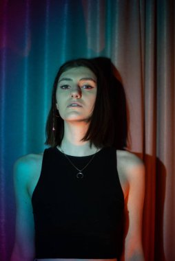 Kot pantolon ve siyah tişörtlü genç ve seksi kadın renkli neon ışıkta poz veriyor.