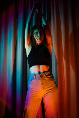 Kot pantolon ve siyah tişörtlü genç ve seksi kadın renkli neon ışıkta poz veriyor.