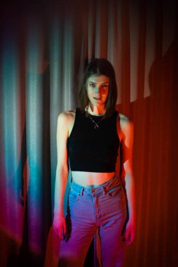 Kot pantolon ve siyah tişörtlü genç ve seksi kadın renkli neon ışıkta poz veriyor.