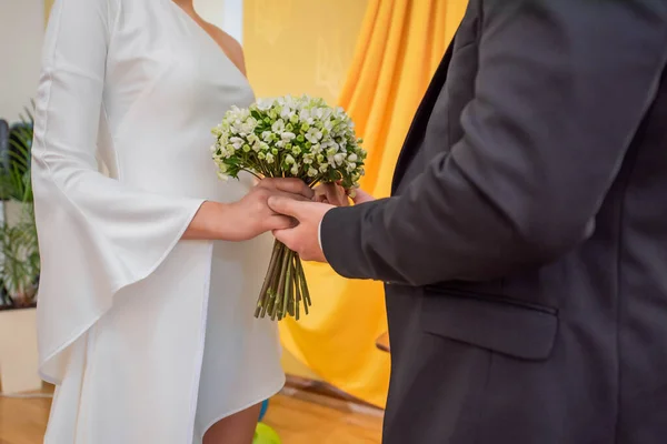 婚礼期间 身穿黑色西服的新郎牵着新娘的手 新娘身穿白色婚纱 山谷中一束小小的百合花 — 图库照片