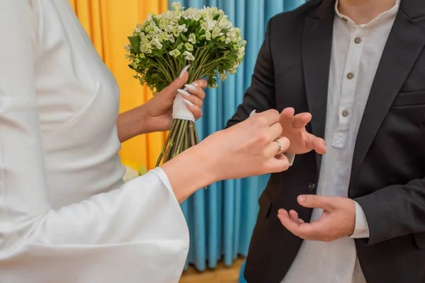 婚礼期间 身穿黑色西服的新郎牵着身穿白色婚纱的新娘的手 一束小花 — 图库照片