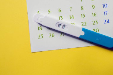 positive pregnancy test with calendar on yellow background