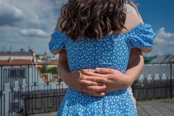 the man holds the girl by the waist. A woman in a blue dress with flowers. city view