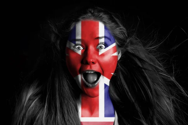 a girl with a British flag on her face is shouting at the camera on a black background