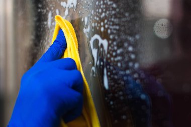 Bir kadın ya da erkek evdeki pencereyi temizler. Ev temizliği. Cam temizleme deterjanı. Mavi eldivenler ve sarı bir bez parçası.