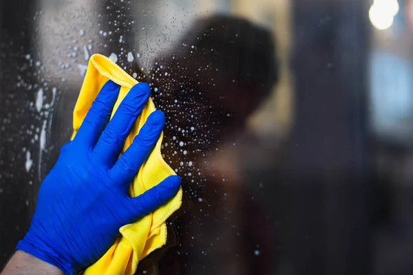 A woman or man washes a window at home. House cleaning. Washing dirty window glass detergent for window washing wearing blue mittens and a yellow cloth rag