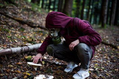 a man in a gas mask sits in the middle of the forest and touches a mushroom. nuclear war concept