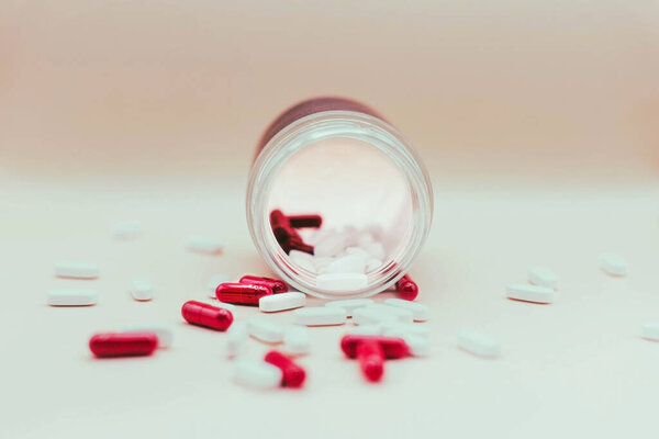 красные и белые таблетки, падающие из банки на белом фоне