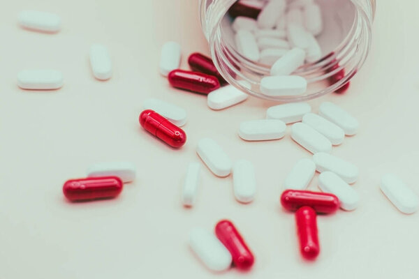 красные и белые таблетки, выпадающие из открытой банки на белом фоне