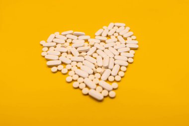 Heart made of white pills on color yellow background