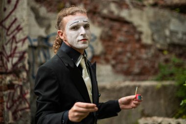Man mime with a painted face stands with a paintbrush in his hands