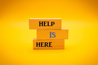 HELP IS HERE text written on wood block yellow background