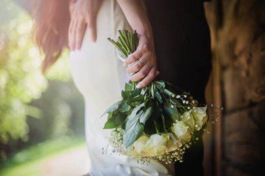 the groom hugs the waist of the bride in a white dress. hugging newlyweds close-up. bride holding white roses flowers in her hand