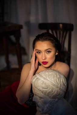 Siyah saçlı, kahverengi gözlü ve vahşi bakışlı bir kadın heykelin başında oturur ve kameraya bakar. Portre.