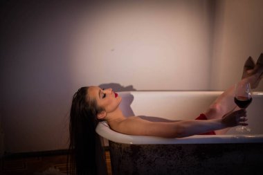 Uzun siyah saçlı çekici kadın banyoda yatıyor. Kırmızı bir elbise giymiş ve elinde bir bardak kırmızı şarap tutuyordu. Bacaklarını küvetin üstüne attı..