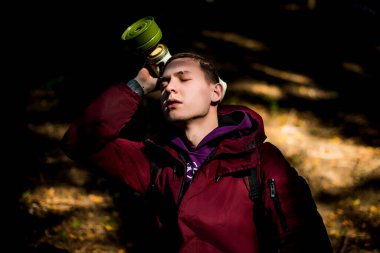 Kırmızı ceketli, şık bir genç. Bir adam elinde gaz maskesi tutuyor. Güneş onun yüzünde parlıyor. Arka planda orman var. Sonbahar mevsimi.