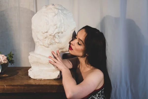 A brunette with red lips leaned against a white statue. gentle horizontal image.