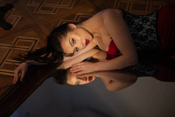 Kırmızı Elbiseli Parlak Makyajlı Bir Esmer Aynanın Yanında Yerde Yatıyor — Stok fotoğraf