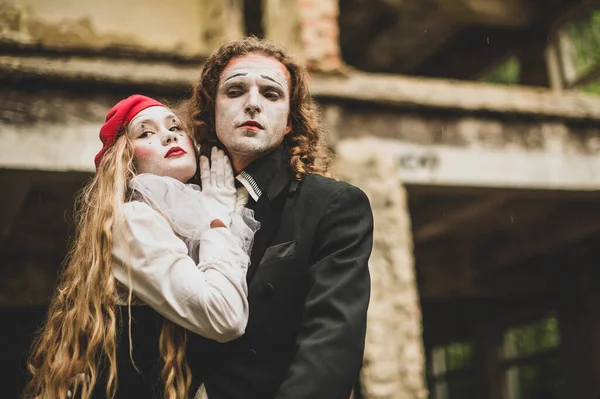 A girl in a black and white suit in a red beret with make-up leans on a tall young man in a black suit and hat. On the background of a dilapidated house. Celebration, Halloween. Close up. Portrait