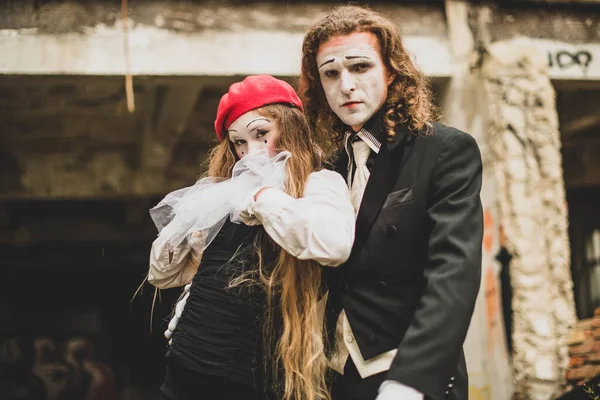 A girl in a black and white suit in a red beret with make-up leans on a tall young man in a black suit and hat. On the background of a dilapidated house. Celebration, Halloween. Close up. Portrait