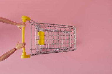 Kukla eller pembe arka planda bir süpermarketten tramvayı itiyor, minimalizm kavramı.