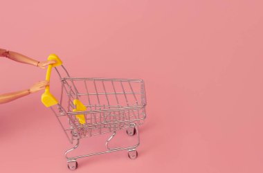 Kukla eller pembe arka planda bir süpermarketten tramvayı itiyor, minimalizm kavramı.