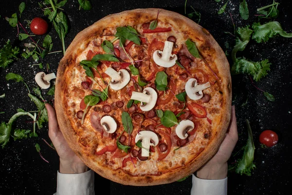 Вид сверху на аппетитную классическую пиццу с сыром, оливковым маслом и свежими овощами на темно-черном столе Стоковое Фото