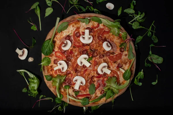 Вид сверху на аппетитную классическую пиццу с сыром, оливковым маслом и свежими овощами на темно-черном столе Лицензионные Стоковые Изображения