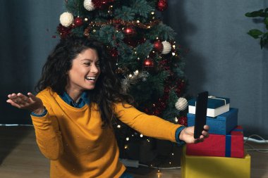 Genç bir kadın, Noel ağacının önünde yerde oturup video üzerinden erkek arkadaşıyla konuşuyor. Yeni yıl tatilinde evde olamayacak bir askerle. 