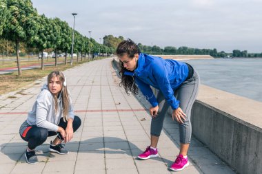 İki genç, mutlu ve kendini beğenmiş sportif koşucu kadın. Koşu yaptıktan sonra en iyi arkadaşlar. Vücut ağırlığı egzersizi yapmak ve antrenman yapmak için nehrin kenarında koşuyorlar. 