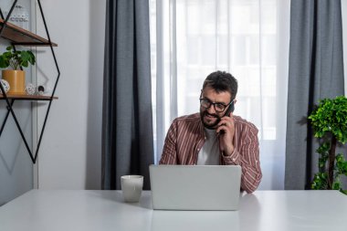 Gözlüklü gülümseyen işadamı telefonla konuşuyor, dizüstü bilgisayarla masada oturuyor, arkadaş canlısı yönetici müşteriye telefonla danışıyor, işten kaytaran arkadaşlarıyla sohbet eden mutlu bir adam.