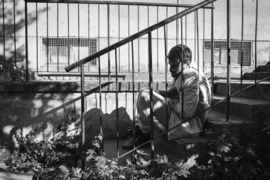 Aç, hasta ve bunalımlı genç adam yemek aradıktan sonra dinlenmek ve kalabalığın dışında kalmak için şehrin caddesindeki merdivenlerde oturuyor. Sosyal belgesel konsepti.