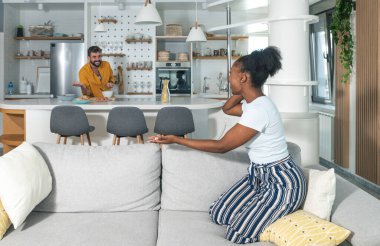 Evlerindeki genç melez çift telefonda konuşuyor ve mutlu çünkü iyi haberler almış ve bir adam mutfakta durup gülüyor yemek pişirirken, seçici bir şekilde odaklanıyor.