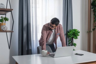 Mutsuz işadamı ayakta duruyor ve stresle dizüstü bilgisayara bakıyor. Ofiste iş projesinde sorun yaşıyor. Genç adam işinden memnun değil, teslim tarihine yetişemiyor.