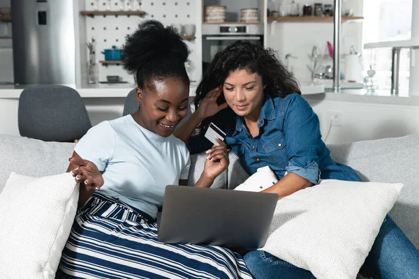 Two happy carefree young women business partners and friends sitting on the sofa are happy because they have just tried online shopping with credit cards on their new internet store website