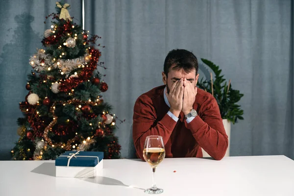 坐在桌旁的一个压力很大的年轻人忘了服用药丸来缓解焦虑 但他开始喝香槟 他很害怕 因为他需要去参加圣诞晚会 — 图库照片