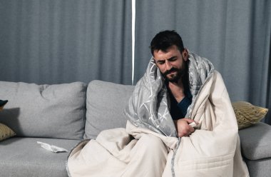 Genç bir adam evde üşütmüş, ateşi çıkmış, grip virüsü kapmış kanepede oturmuş boğazı ağrıyan bir şekilde yatıyor. 