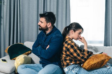 Genç çift evlerindeki kanepede tartışıyor ve ilişkilerinde ve evliliklerinde zorluk ve sorunlar yaşıyor sırt sırta oturuyor görmezden geliyor ve birbirleriyle konuşmuyorlar, ilişki sorunları var.
