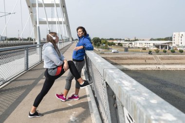 İki genç mutlu ve kendini beğenmiş koşu kadını. En iyi arkadaşlar, koşudan sonra kaslarını esnetmeye ara verip sağlıklı bir yaşam için sonbaharda açık havada vücut ağırlığı egzersizi ve antrenman yapıyorlar. 