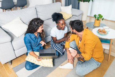 Üç mutlu arkadaş, yerde oturup eğlenirken bir kredi kartı ve dizüstü bilgisayarla online alışveriş yapıyorlar. Restorandan online yiyecek ve içecek sipariş eden arkadaşlar..