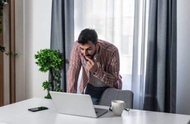 Şirketinin olumlu istatistiklerini okuyup gülümseyen, modern ev ofisinin çalışma yerinde dizüstü bilgisayarla çalışan mutlu genç iş adamı işten memnun.