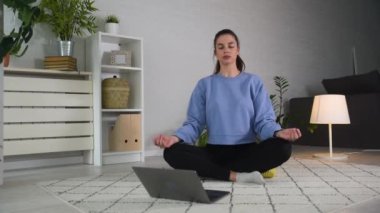 Nilüfer çiçeğiyle poz veren sakin kadın dizüstü bilgisayarının yanında tek başına yerde meditasyon yapıyor. Kadın oturma odasında derin ve rahatlatıcı nefes alma egzersizleri yapıyor. Kadın derin nefes alıp veriyor..