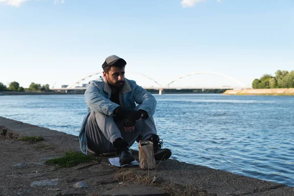 Çaresizlik içinde, evsiz bir adam terk edilmiş ve üzgün bir şekilde dışarıda oturuyor. İşsiz hasta erkeğin yardıma ihtiyacı var. Evsizlik sosyal meseleler kavramı.