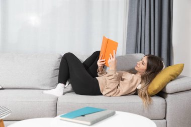 Genç ve güzel bir kadın rahat evinde kanepede oturmuş kitap okuyor ve kocası ve çocukları olmadan mutlu yüzüyle boş zamanlarının tadını çıkarıyor. Kız öğrenci çalışması ve rahatlatıcı..