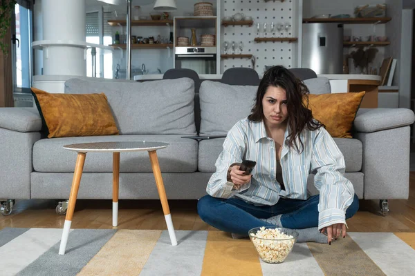 Young shocked vegetarian woman sitting at home watching television changing the program after she saw animal brutality. Unhappy female with disgusting facial expression pressing tv remote button.